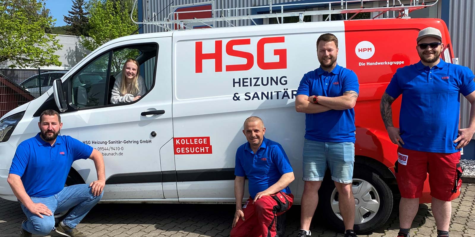 Eine Gruppe von vier Handwerkern in blauen T-Shirts posiert vor einem weißen Lieferwagen mit dem Logo von HSG Heizung & Sanitär.