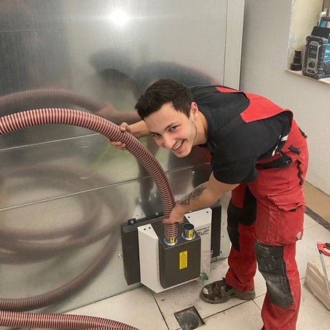 Ein junger Handwerker mit einem breiten Lächeln verbindet einen Schlauch mit einer Maschine in einem modernen Raum.