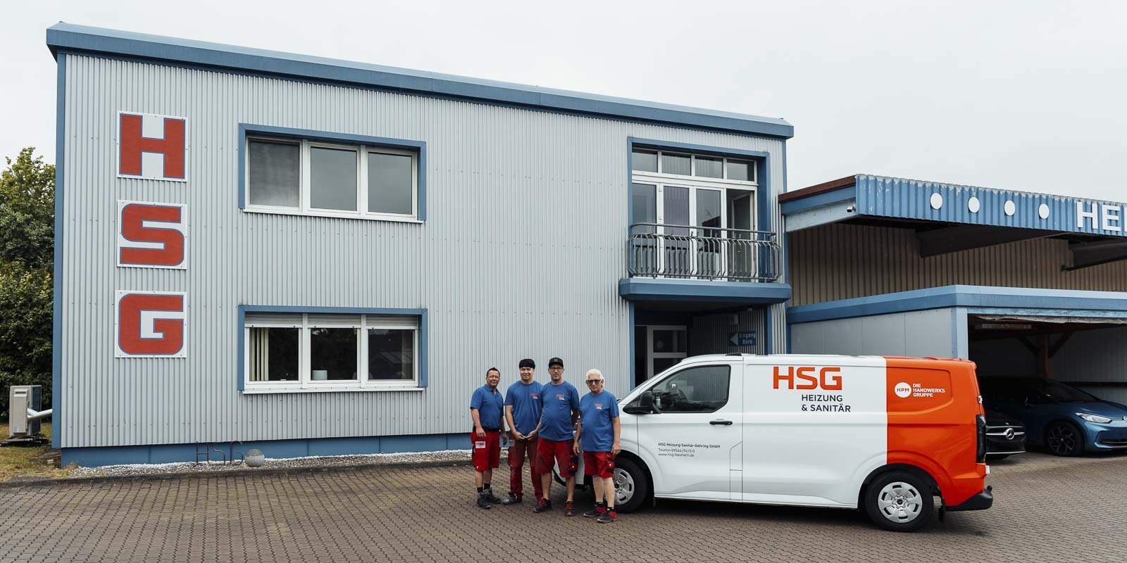 Das Team von HSG Heizung & Sanitär posiert vor ihrem Firmengebäude, das mit großen roten Buchstaben beschriftet ist.