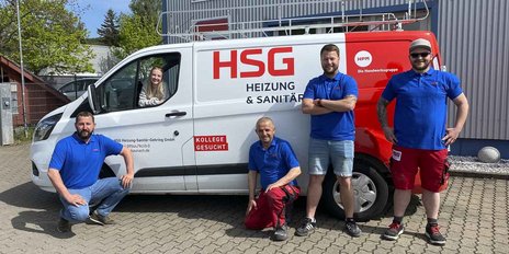 Ein Team von vier Handwerkern in blauen T-Shirts posiert vor einem weißen Lieferwagen mit dem Logo von HSG Heizung & Sanitär.