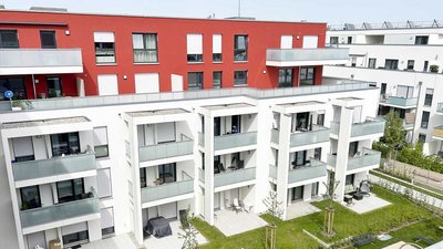Moderne Wohnanlage mit roten und weißen Fassaden, Balkonen und begrünten Außenbereichen, die eine einladende Atmosphäre schaffen.