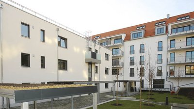 Ein moderner Innenhof mit mehreren Wohngebäuden, die große Fenster und Balkone aufweisen, umgeben von gepflegtem Grün.