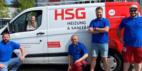 Eine Gruppe von vier Handwerkern in blauen T-Shirts posiert vor einem weißen Lieferwagen mit dem Logo von HSG.