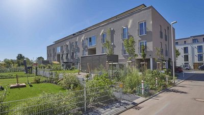 Moderne Wohngebäude mit großen Fenstern und einem gepflegten Gartenbereich, umgeben von Bäumen und Sträuchern.