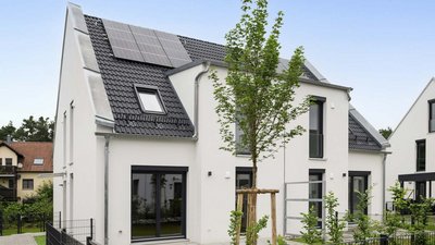 Ein modernes, zweigeschossiges Haus mit Solarpanelen auf dem Dach und großen Fenstern, umgeben von frischem Grün.