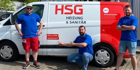 Drei Männer in blauen T-Shirts stehen vor einem weißen Lieferwagen mit der Aufschrift 'HSG Heizung & Sanitär'.